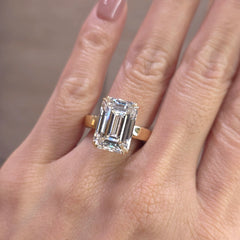 An emerald-cut diamond ring on a yellow gold band, shown worn on a person's finger.