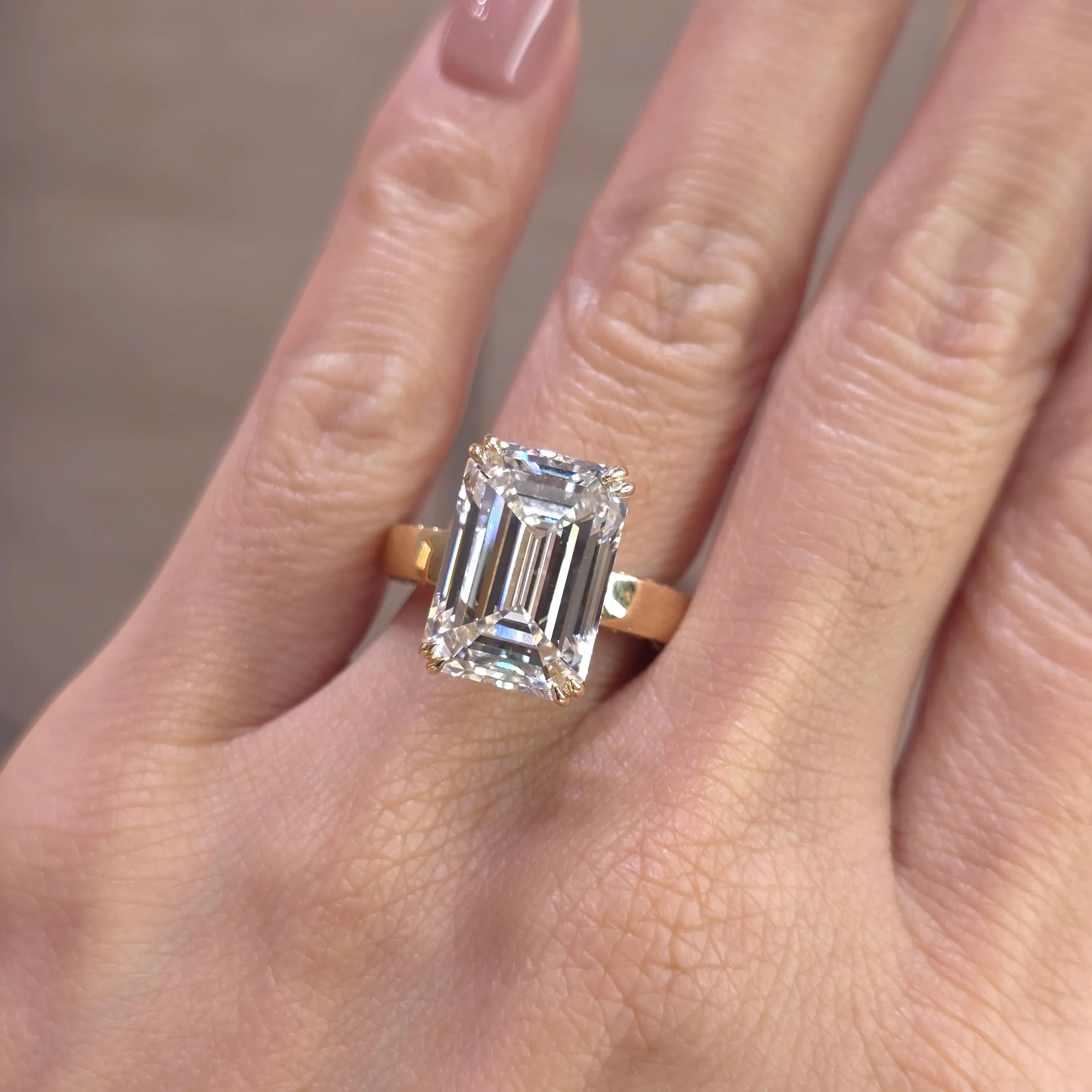 An emerald-cut diamond ring on a yellow gold band, shown worn on a person's finger.