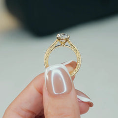 Elegant gold engagement ring with lab-grown diamond and intricate filigree band, held delicately in hand.