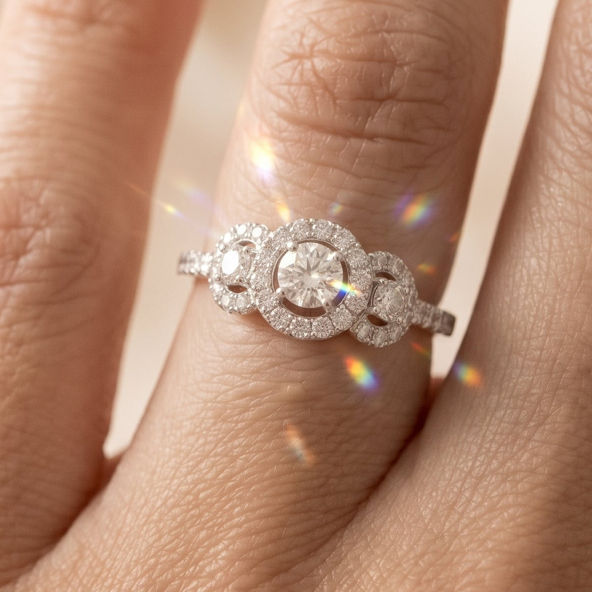 A close-up of a hand wearing a silver-toned ring with a three-stone oval cluster design set with clear gemstones, showing sparkling light reflections.